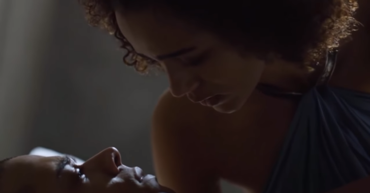  A screenshot of Game of Thrones, series 5 (2014). Grey Worm is wounded and lying in bed. Missandei leans over to kiss him for the first time. They are backlit, creating a soft glow along their features.